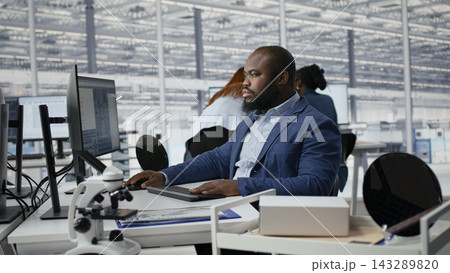 Examining microchip circuit layouts, computer monitor and man in factory RD office using specialized software. Improving manufacturing, semiconductors used in smart device sand African american worker Examining microchip circuit layouts, computer monitor and man in factory RD office using specialized software. Improving manufacturing, semiconductors used in smart device sand African american worker 143289820