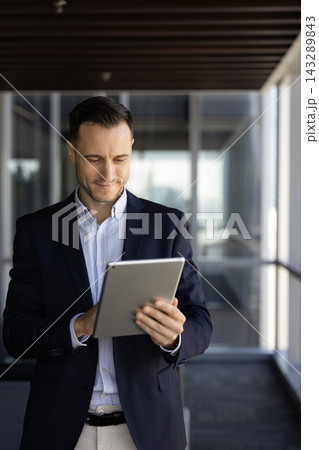Focused businessman using digital tablet stands alone in office hallway 143289843