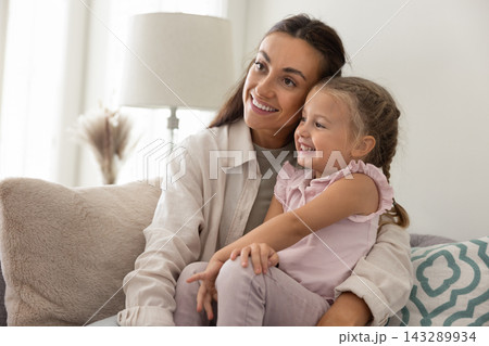 Affectionate mother relaxing on cozy sofa hugging little daughter dreaming 143289934