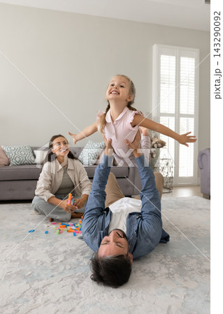 Smiling mom watch laughing dad holding toddler daughter in air Smiling mom watch laughing dad holding toddler daughter in air 143290092