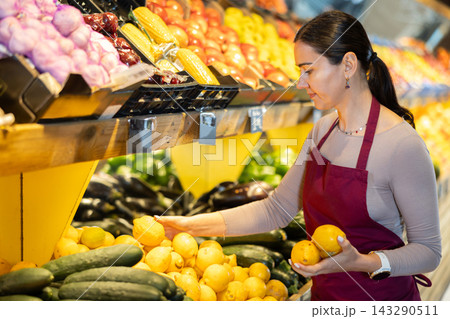 Female salesperson carefully places ripe lemons on the counter of grocery supermarket Female salesperson carefully places ripe lemons on the counter of grocery supermarket 143290511