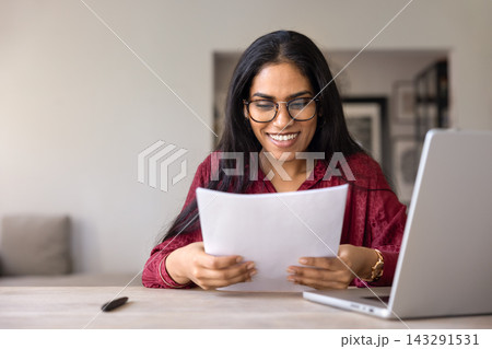 Indian woman reading documents with contented smile Indian woman reading documents with contented smile 143291531