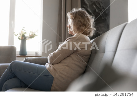 Peaceful senior woman sitting by window looking outside thoughtfully Peaceful senior woman sitting by window looking outside thoughtfully 143291754
