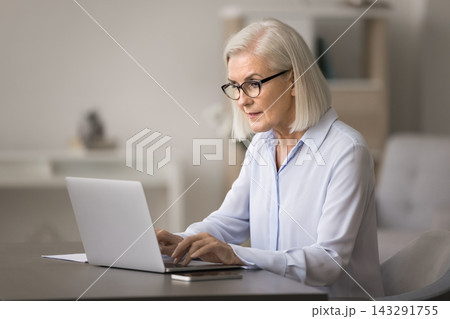 Serious concentrated older age businesswoman type document on laptop 143291755