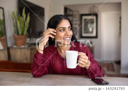 Smiling Indian woman sit at table with mug Smiling Indian woman sit at table with mug 143291793