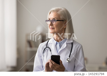 Thoughtful older woman medic use phone at work look aside Thoughtful older woman medic use phone at work look aside 143291794