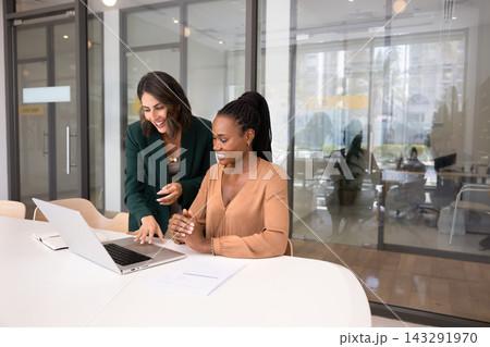 Smiling Hispanic woman explaining project details on laptop to colleague 143291970