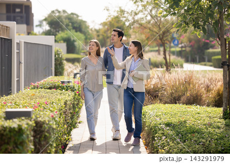 Realtor and clients walking along well-groomed garden in residential complex 143291979