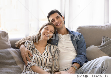 Portrait of young couple hugging seated together on cozy sofa Portrait of young couple hugging seated together on cozy sofa 143292015