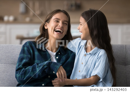 Woman and daughter laughing while talking seated on couch 143292403