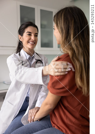 Female doctor gently touches shoulders, supporting woman patient Female doctor gently touches shoulders, supporting woman patient 143293211