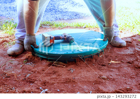 Worker places green cover over wastewater treatment tank in backyard Worker places green cover over wastewater treatment tank in backyard 143293272