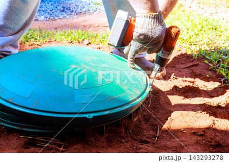 Builder is using drill to secure green cover on utility box in garden. Builder is using drill to secure green cover on utility box in garden. 143293278