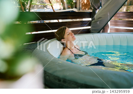 Woman relaxing in inflatable hot tub on outdoor terrace 143295959
