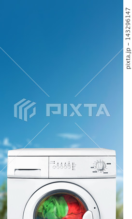 A close-up shot of a white front-load washing machine with green and red laundry inside, set against a bright blue sky background. Quotes background A close-up shot of a white front-load washing machine with green and red laundry inside, set against a bright blue sky background. Quotes background 143296147