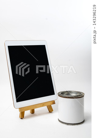 A blank tablet on a wooden easel next to a blank white paint can on a white surface, ideal for design mockups. A blank tablet on a wooden easel next to a blank white paint can on a white surface, ideal for design mockups. 143296219