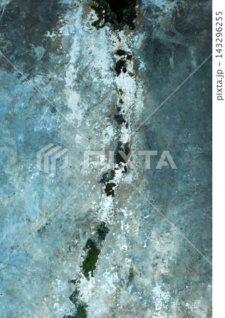 An aged, weathered concrete surface featuring a distinct vertical crack filled with white efflorescence and patches of green moss, creating a textured industrial backdrop. Textured background 143296255