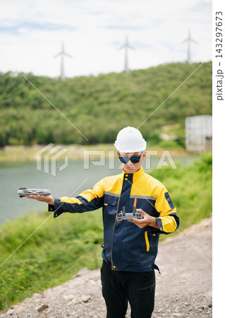 Asian engineer in hardhat landing a drone on his hand near wind turbines for renewable energy site inspection and survey. Asian engineer in hardhat landing a drone on his hand near wind turbines for renewable energy site inspection and survey. 143297673