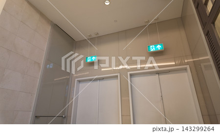Exit signs provide guidance to the doors located along a building's hallway Exit signs provide guidance to the doors located along a building's hallway 143299264