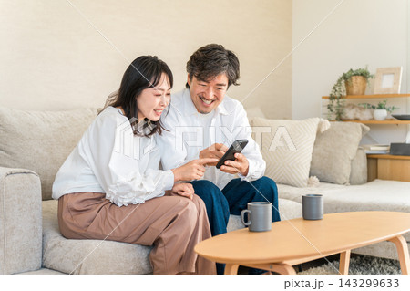 スマホを一緒に見ながら情報収集する40代の夫婦。家計や資産運用を考えるミドル世代 スマホを一緒に見ながら情報収集する40代の夫婦。家計や資産運用を考えるミドル世代 143299633