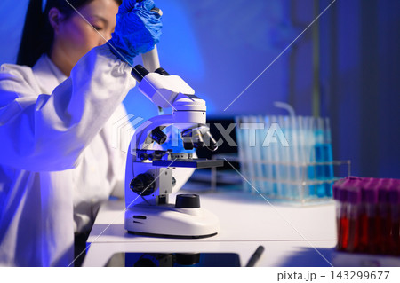 Female Scientist Using Microscope in Blue Lit Research Laboratory with Test Tubes and Samples 143299677