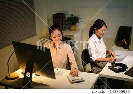 Two Young Businesswomen Working Late at Night in Office with Computer and Calculator 143299680