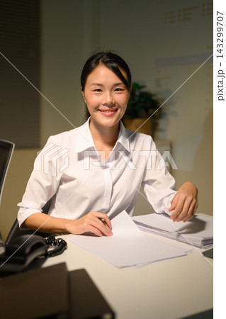Smiling Young Businesswoman Working at Office Desk with Documents and Phone Smiling Young Businesswoman Working at Office Desk with Documents and Phone 143299707
