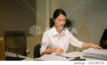 Stressed Businesswoman Working Late at Night Sorting Through Pile of Documents at Office Desk Stressed Businesswoman Working Late at Night Sorting Through Pile of Documents at Office Desk 143299730