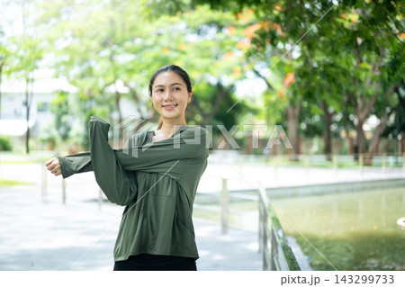 Young Asian Woman Stretching Arms in Green Park Before Workout Outdoors 143299733