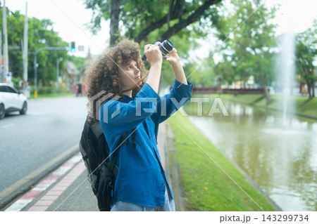 Young Female Traveler with Curly Hair Photographing with Film Camera in Asian City Park Young Female Traveler with Curly Hair Photographing with Film Camera in Asian City Park 143299734
