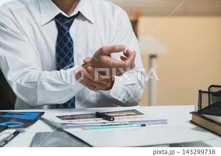 Businessman Sitting at Desk with Clasped Hands Over Financial Charts in Office 143299736