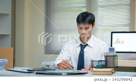 Businessman Working at Office Desk Reviewing Financial Charts and Documents with Pen 143299842