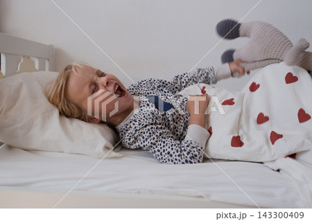 Angry little girl crying and throwing stuffed toy in bed Angry little girl crying and throwing stuffed toy in bed 143300409