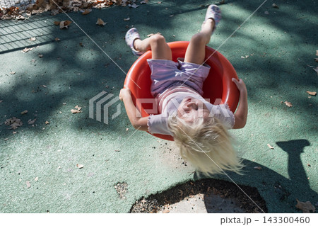 little girl spinning upside down in bowl roundabout seat at outdoor playground little girl spinning upside down in bowl roundabout seat at outdoor playground 143300460
