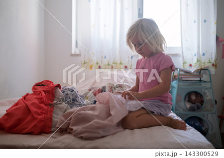 Little Girl Sorting Clean Laundry on the Bed Little Girl Sorting Clean Laundry on the Bed 143300529