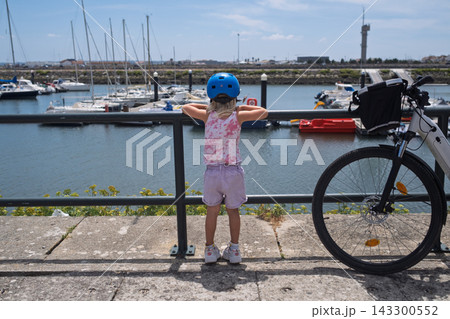 Little Girl Looking at Yachts in the Marina Next to a Bicycle Little Girl Looking at Yachts in the Marina Next to a Bicycle 143300552