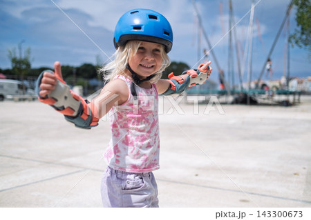 Cute Blonde Toddler in Safety Equipment Giving Thumbs Up Gesture Outdoors 143300673