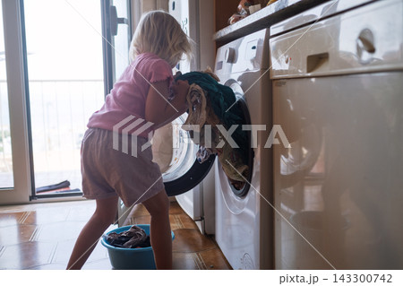 Little Girl Loading Clothes into the Washing Machine at Home Little Girl Loading Clothes into the Washing Machine at Home 143300742