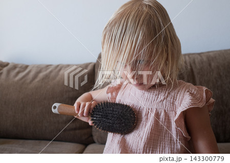 girl in a pink dress brushing her damp hair on a brown couch. girl in a pink dress brushing her damp hair on a brown couch. 143300779