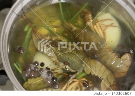 Live green crayfish boiling in a metal pot with water, spices, herbs, and vegetables, cooking delicious traditional seafood soup on the stove. Live green crayfish boiling in a metal pot with water, spices, herbs, and vegetables, cooking delicious traditional seafood soup on the stove. 143301607