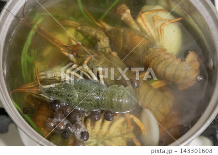 Live green crayfish boiling in a metal pot with water, spices, herbs, and vegetables, cooking delicious traditional seafood soup on the stove. Live green crayfish boiling in a metal pot with water, spices, herbs, and vegetables, cooking delicious traditional seafood soup on the stove. 143301608