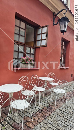 Terracotta architecture features open wooden windows above ornate white cafe tables and chairs, with a traditional wall lantern beside cobblestones Terracotta architecture features open wooden windows above ornate white cafe tables and chairs, with a traditional wall lantern beside cobblestones 143301678