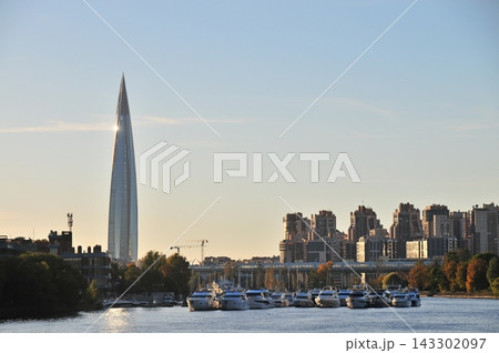 White yachts moored along riverbank with glass skyscraper piercing sky, modern city skyline at golden hour, urban waterfront architecture White yachts moored along riverbank with glass skyscraper piercing sky, modern city skyline at golden hour, urban waterfront architecture 143302097