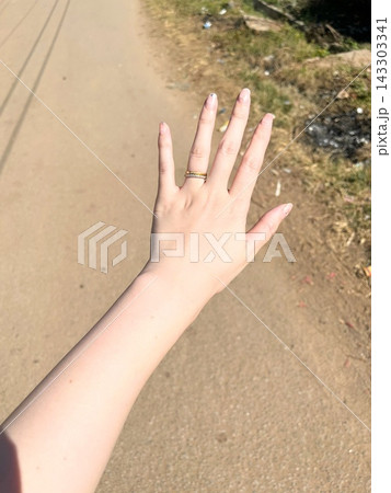 指輪をつけた女性の手元と伸ばされた腕および背景に広がる屋外の道路と草地がある風景 143303341