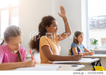 Black schoolgirl raising her hand to answer question during classroom lesson Black schoolgirl raising her hand to answer question during classroom lesson 143303998
