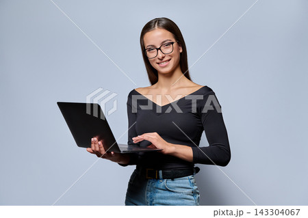 Young woman in glasses holding laptop and looking at camera in studio Young woman in glasses holding laptop and looking at camera in studio 143304067