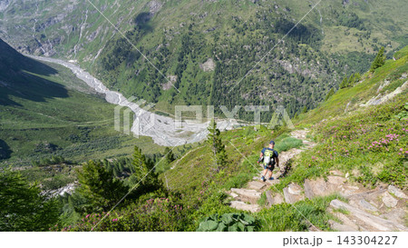 Hiker ascending steep rocky trail in Hohe Tauern National Park Austria with glacial valley and river below 143304227