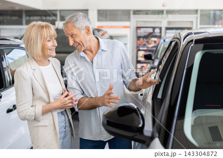 Senior Caucasian couple examining car closely in dealership showroom 143304872