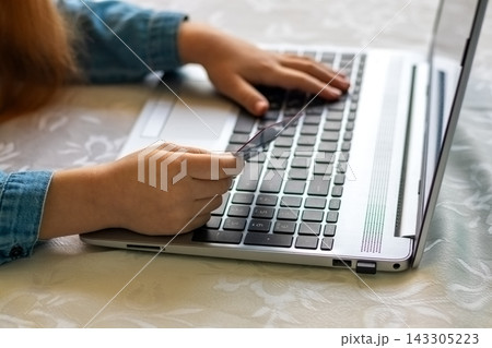Child holding credit card while making online payment on laptop at home Child holding credit card while making online payment on laptop at home 143305223