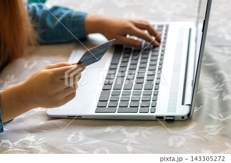 Young child making an online purchase with a credit card while using a laptop at home Young child making an online purchase with a credit card while using a laptop at home 143305272